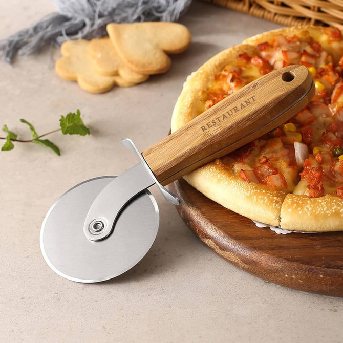 A pizza cutter wheel with a stainless steel blade and a hand-carved wooden handle, alongside a pizza and some biscuits.