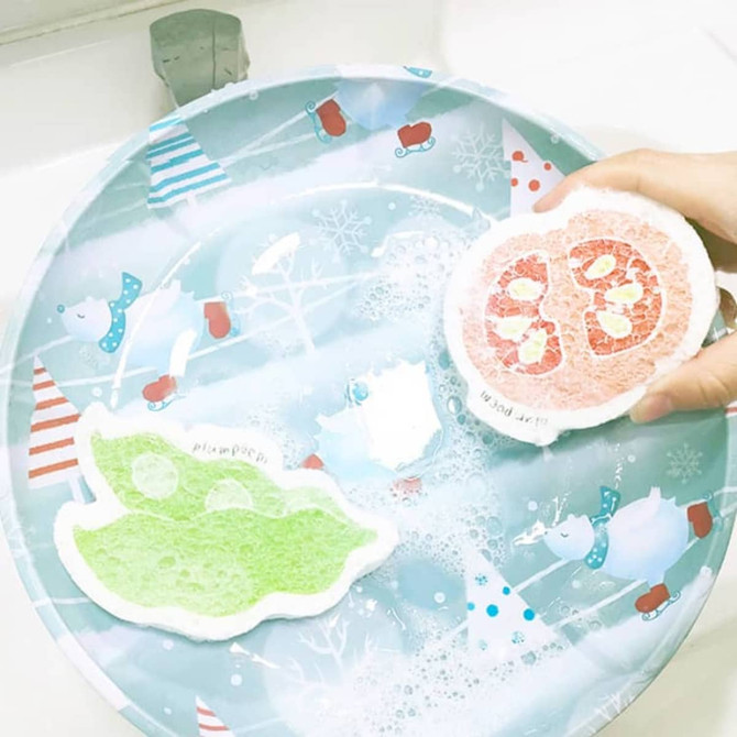 A hand holds two colourful dishwashing sponges on a festive, patterned tray. One sponge is green, and the other is pink.