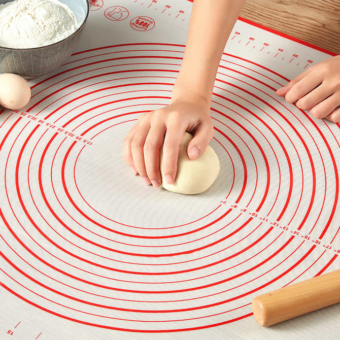 A silicone pastry mat featuring red circular markings, with a hand kneading dough in the centre.