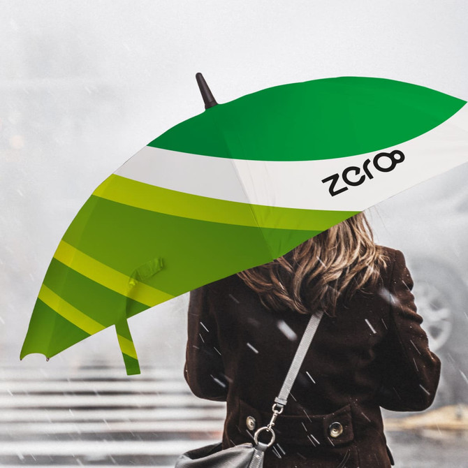 A green and white umbrella with a logo, held by a person with their back turned, against a misty background.
