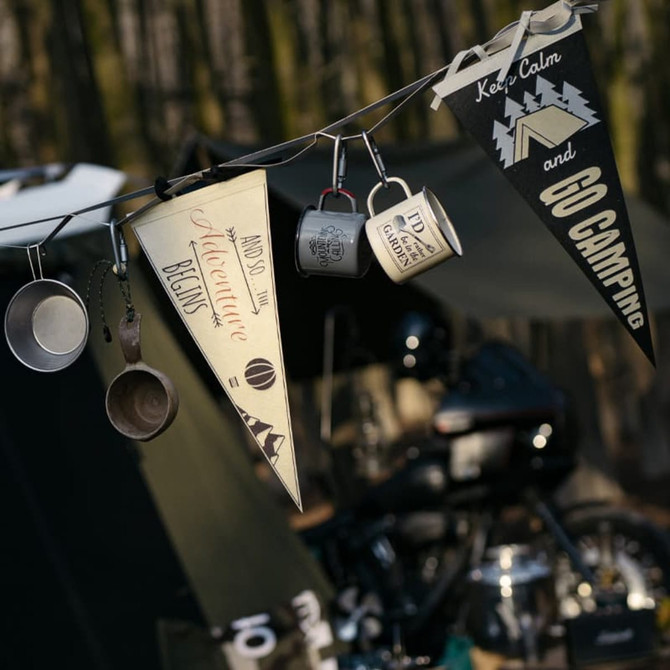 A black and cream felt pennant hanging alongside camping mugs and other camping gear, set outdoors.