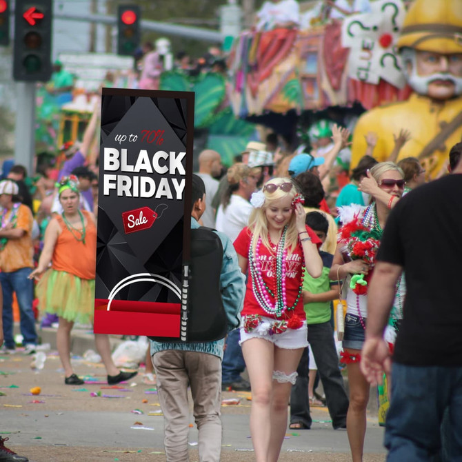 A rectangular backpack flag with a striking black and red design, presented against a busy festive street scene.