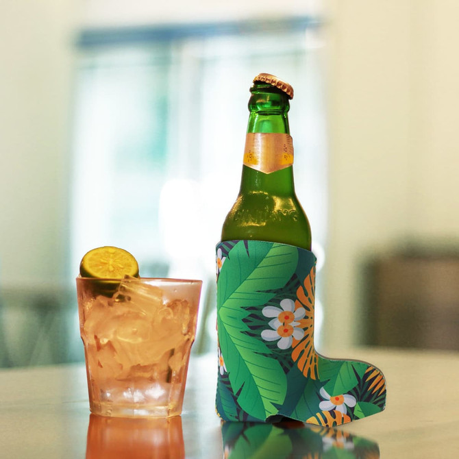 A drink bottle in a vibrant green and floral boot-shaped stubby holder alongside a glass of cocktail with ice.