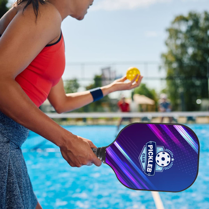 A woman holds a purple and black pickleball paddle, preparing to serve a yellow pickleball on a court.