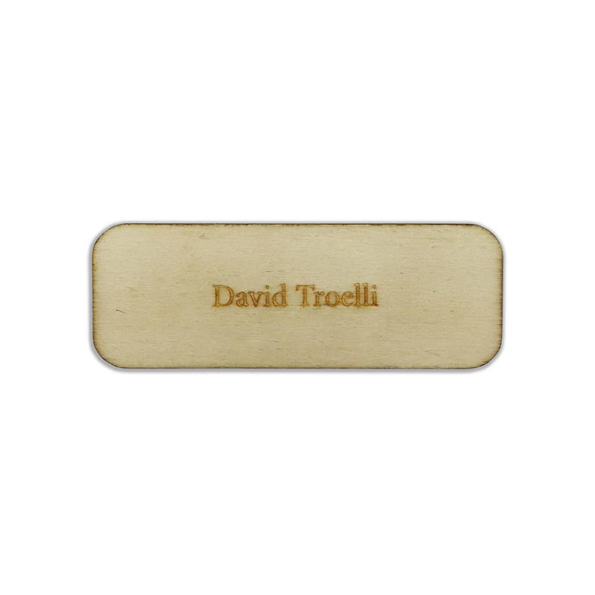 A rectangular wooden badge in light tan with a name engraved on the surface, featuring a subtle, polished finish.