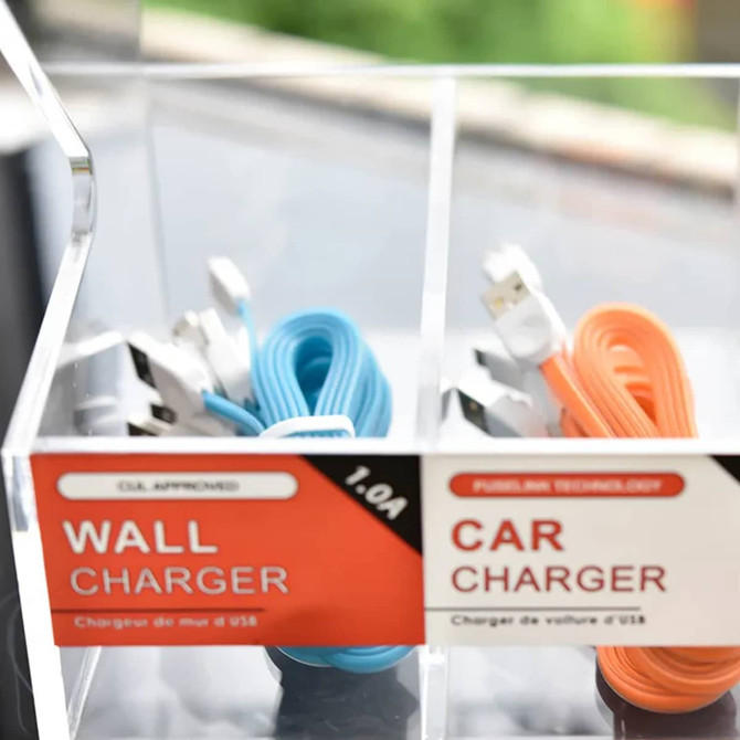 A clear acrylic display with two compartments, featuring blue and orange charging cables and labels for wall and car chargers.