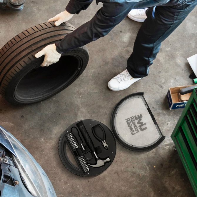 A black car wheel tool kit with various tools, placed beside a person holding a tyre in a workshop setting.