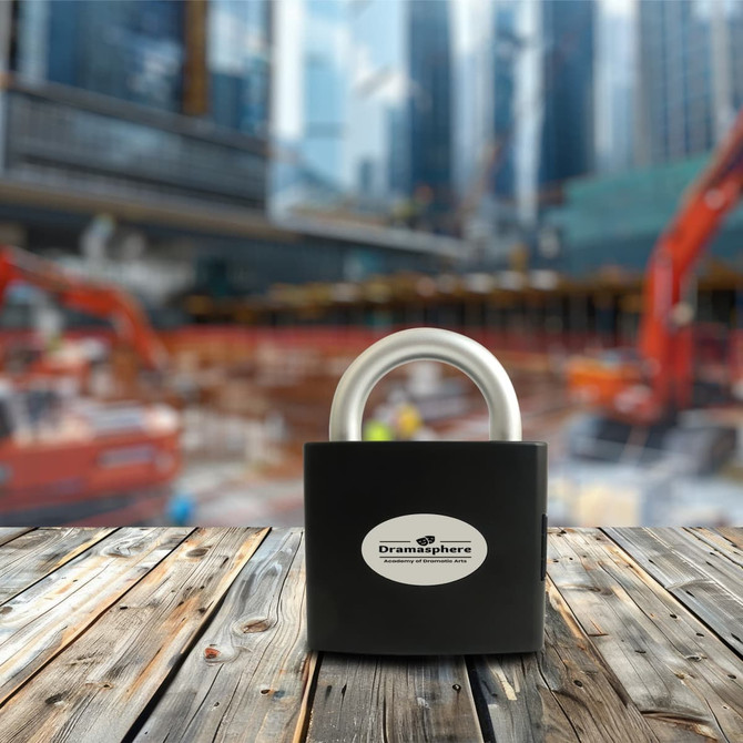 A padlock-shaped toolkit in black, featuring a silver shackle, displayed on a wooden surface with a blurred construction site behind.
