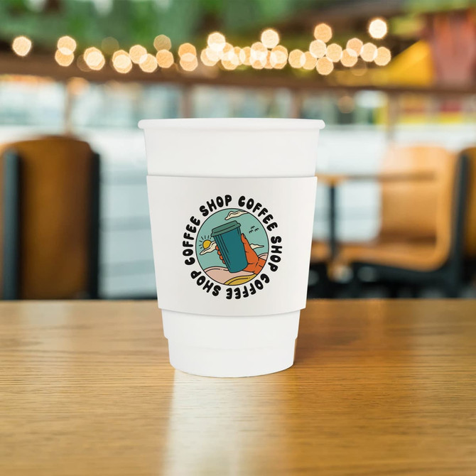 A white double wall paper cup with a cup sleeve, featuring a logo and set on a wooden table in a café.