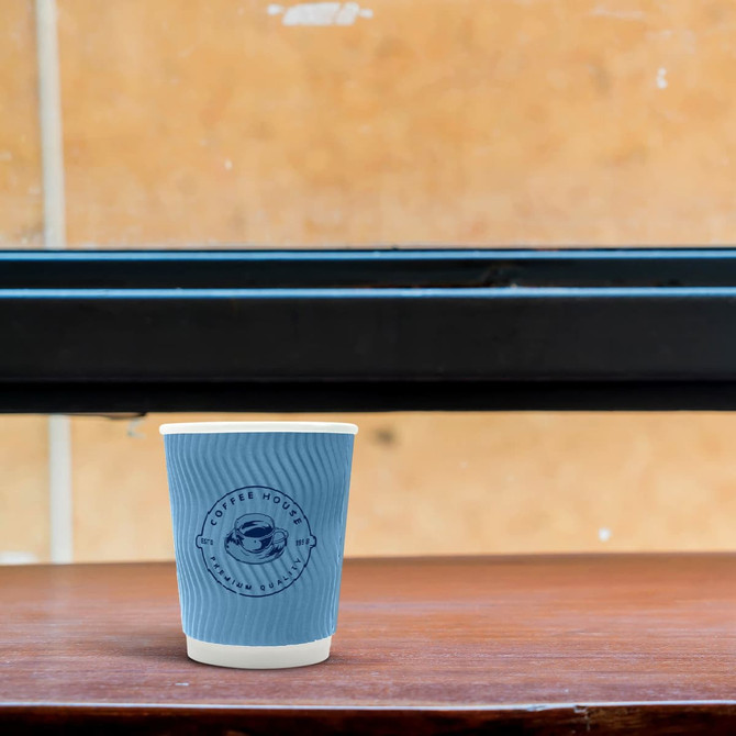 A double wall paper cup in blue, featuring a logo, sits on a wooden table against a textured background.