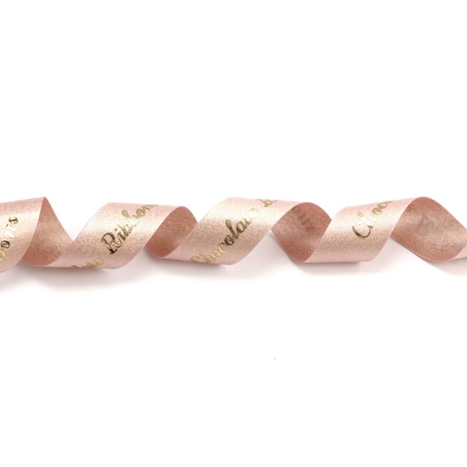 A satin ribbon in glitter gold and soft pink tones, featuring a wavy design and a logo.