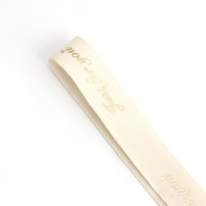 A pale cream cotton ribbon with gold hot stamping and a logo at one end.