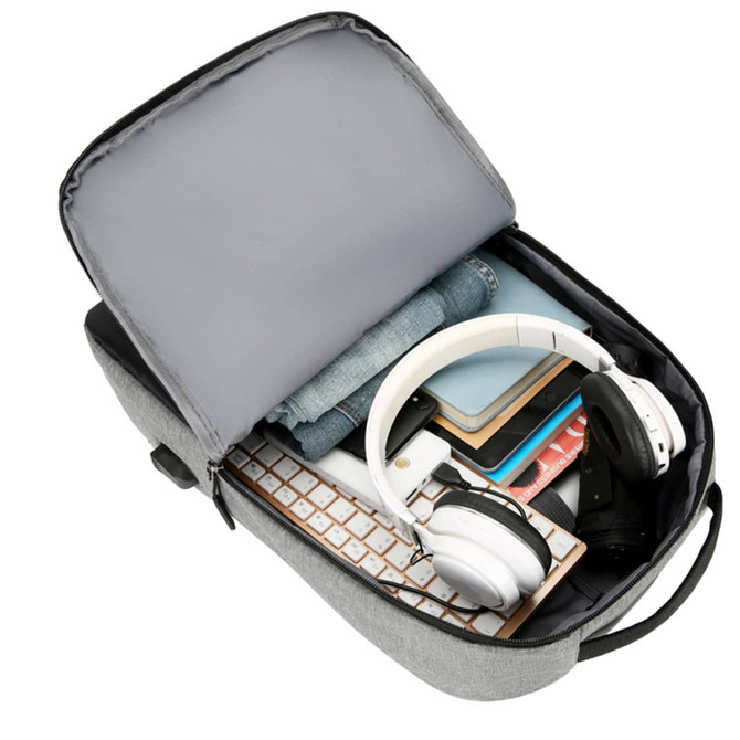 A grey laptop backpack with a USB charging port, packed with headphones, clothing, and various accessories.