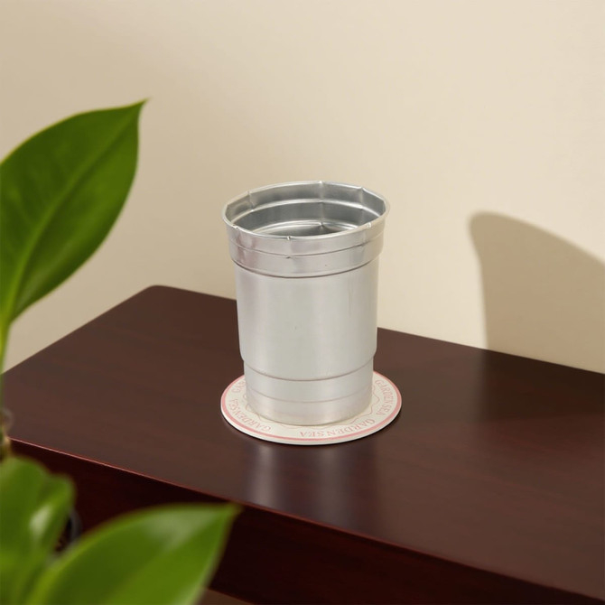 A silver drink bottle sits on a circular PU coaster against a neutral background, with a green plant in the foreground.