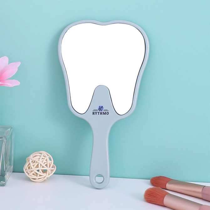 A tooth-shaped face mirror in light grey with a handle, set against a pastel blue background.