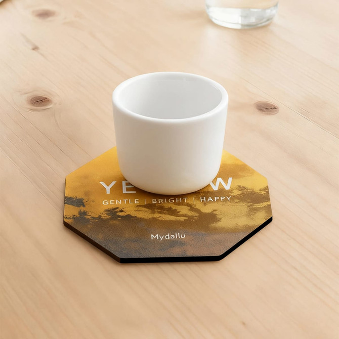 An octagonal frosted metal coaster in yellow and black, featuring a white cup placed on top.