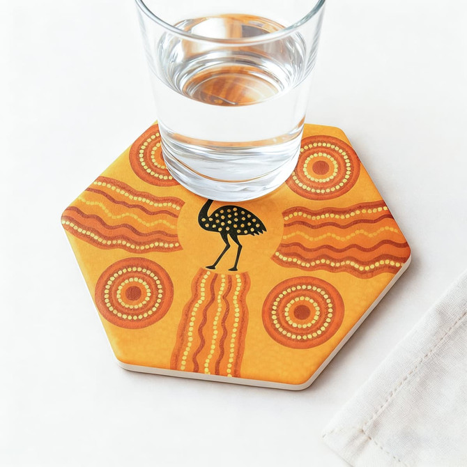 A hexagonal ceramic coaster in orange and yellow with a decorative pattern and a glass of water on top.