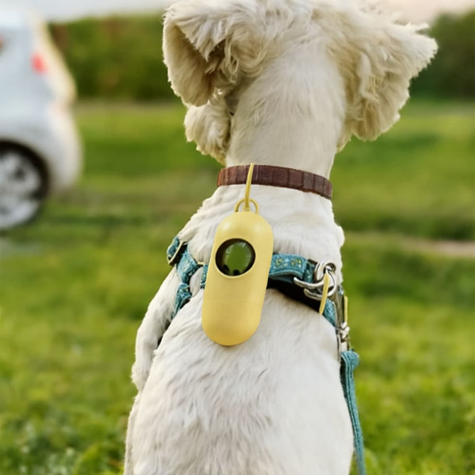 A yellow eco-friendly pet waste bag dispenser attached to a dog's harness in a grassy outdoor setting.