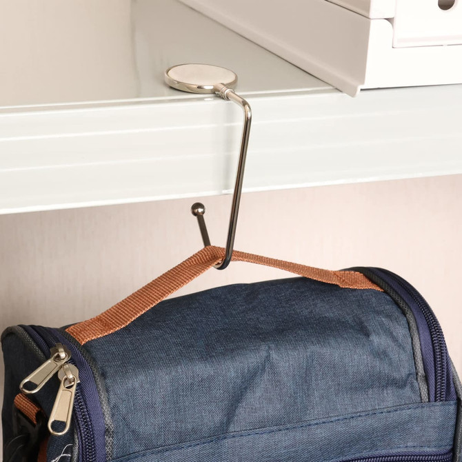 A round, silver desk hook holding a navy backpack, attached to a white shelf above.