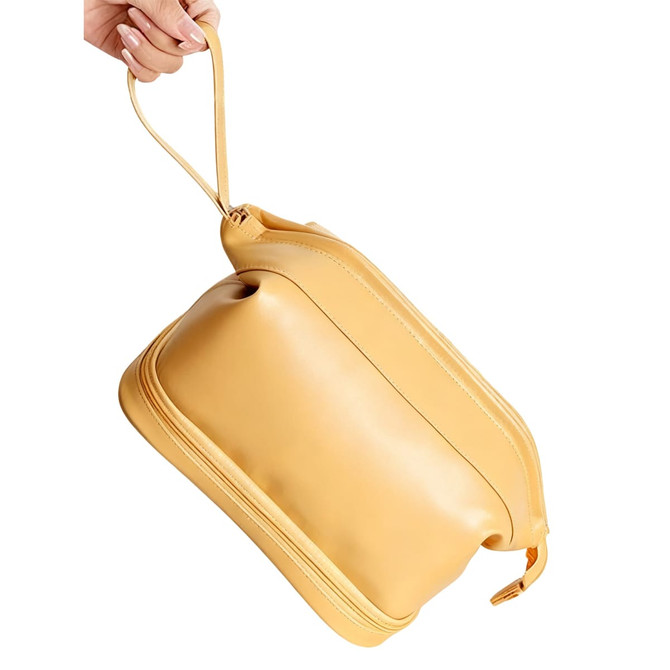 A yellow large capacity PU toiletry bag with a rounded shape and a handle, being held by a hand.