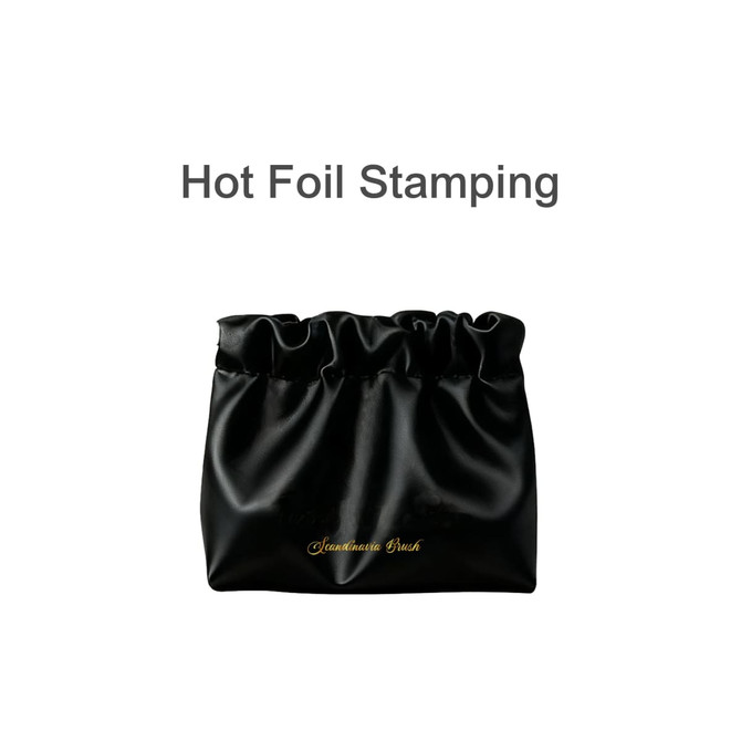 A black zipperless portable makeup bag with a gathered top and gold branding, featuring a smooth satin finish.
