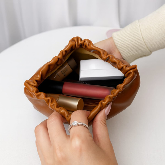 A tan, zipperless portable makeup bag filled with various makeup products, including lipsticks and foundation.