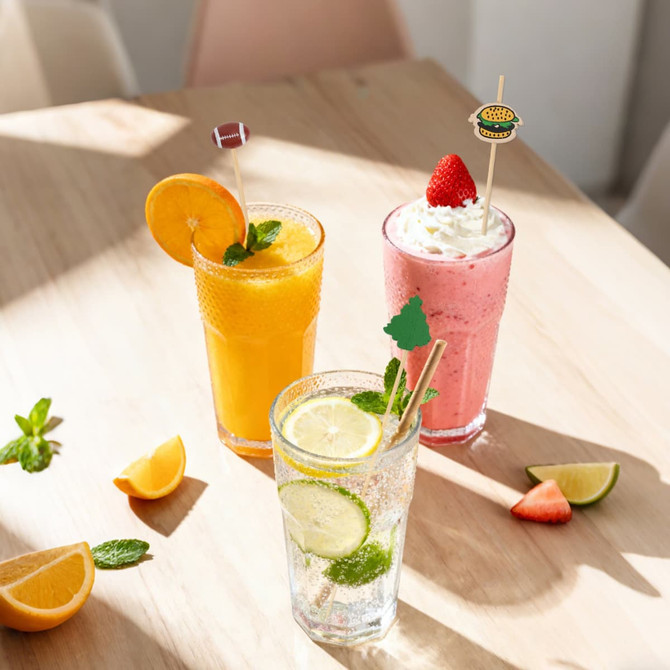 A set of three cocktails in various glasses, featuring orange, strawberry, and lemon garnishes, topped with bamboo skewers.