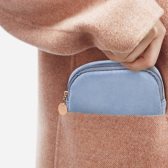 A blue mini makeup bag is partially tucked into the pocket of a pink, knitted sweater. The bag features a zip closure and a small logo.