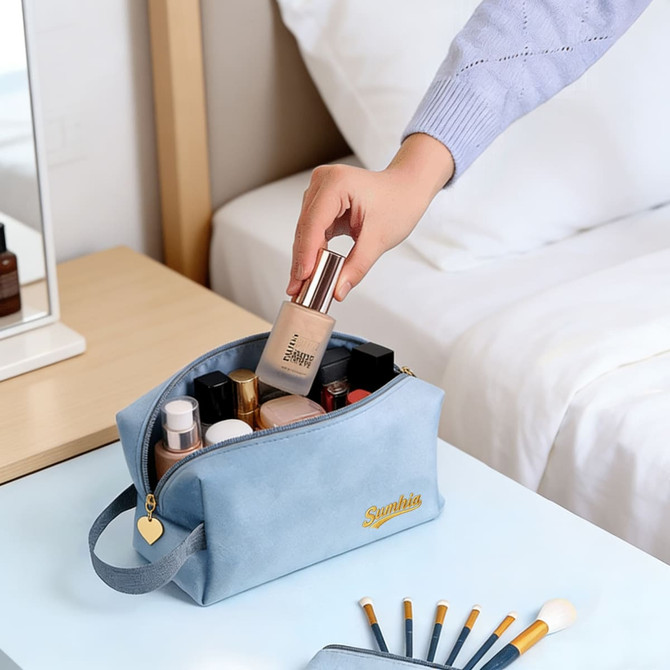 A flannel cosmetic bag in blue, filled with various beauty products, sits on a table beside a bed.