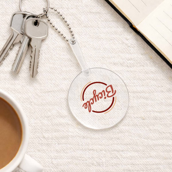A clear PVC hand fan with a keychain, featuring a round shape, sits on a textured surface near a coffee cup and notebook.