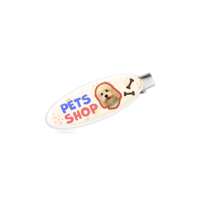 An oval acrylic hair clip featuring a light background, a cute dog image, and colourful "Pets Shop" text.