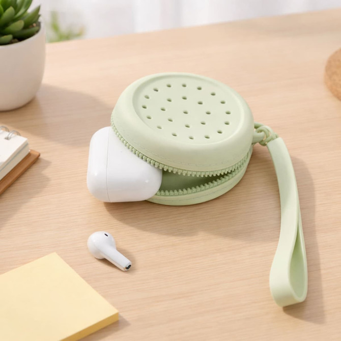 A round silicone pouch in light green, featuring holes, holding wireless earbuds, placed on a wooden surface.