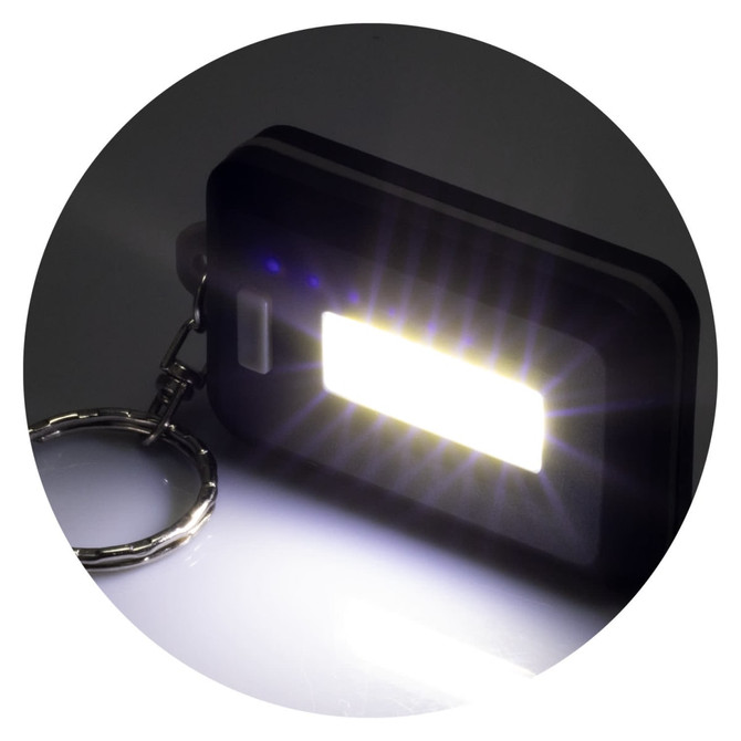 A black key ring light with a rectangular LED panel, emitting a bright white light. It features a metal keychain.