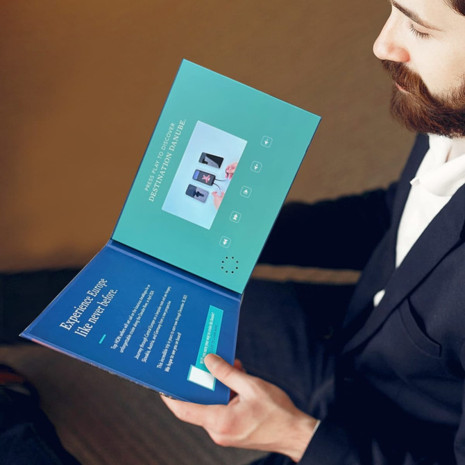 A 4.3-inch LCD video brochure in blue, featuring a play button and display screen, held open by a person.