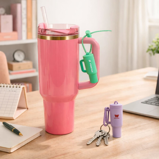 A pink drink bottle with a gold rim, alongside a green and purple lip balm holder keychain on a desk.