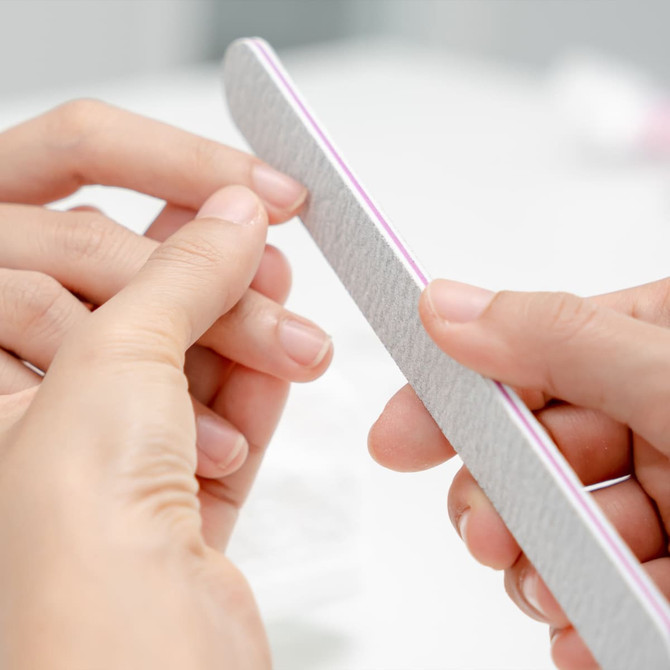 A nail file in use, featuring a straight shape with a light grey surface and a purple edge, held between two hands.