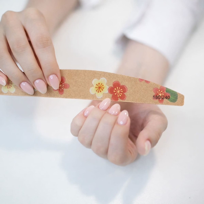 A bamboo nail file with floral designs, held between a person's fingers with freshly manicured pink nails.