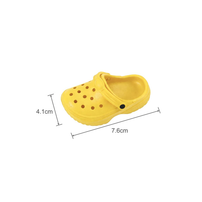 A yellow classic clog shoe fridge magnet with perforations, measuring 7.6 cm by 4.1 cm, featuring a strap and a logo.