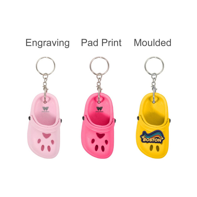 Three keyrings shaped like clogs in pink, pink with a print, and yellow with a logo. All feature metal keyring attachments.