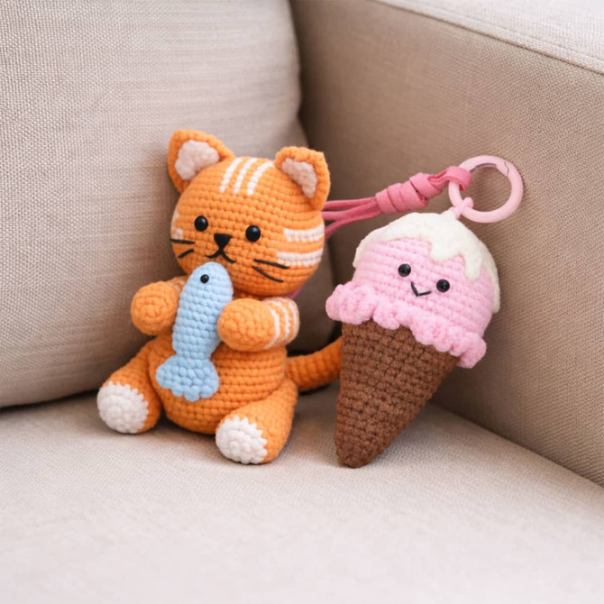 A crochet kit featuring an orange cat holding a fish and a pink ice cream cone with a smiling face.