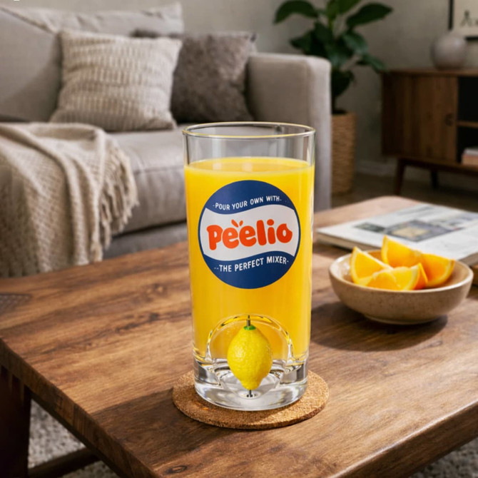 A glass cup filled with orange drink, featuring a lemon slice, on a wooden table with lemon wedges and a cosy living room backdrop.