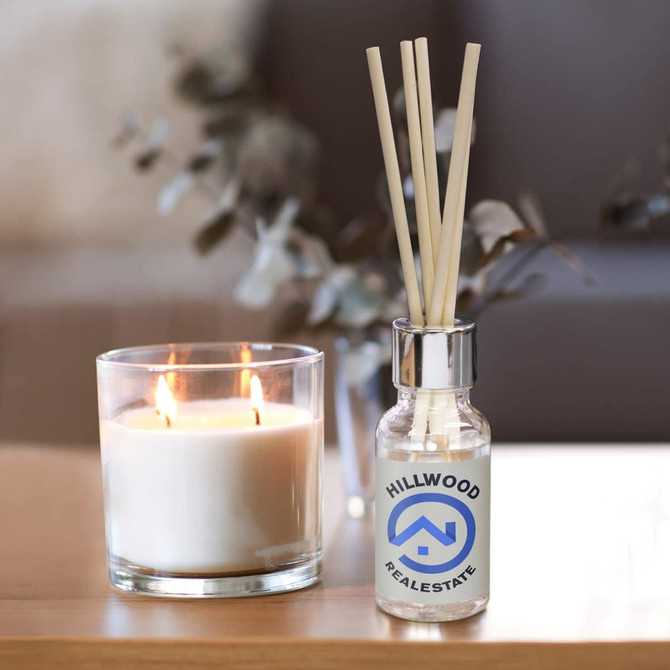 A glass scented diffuser bottle with a silver cap and wooden reeds, alongside a lit glass candle.