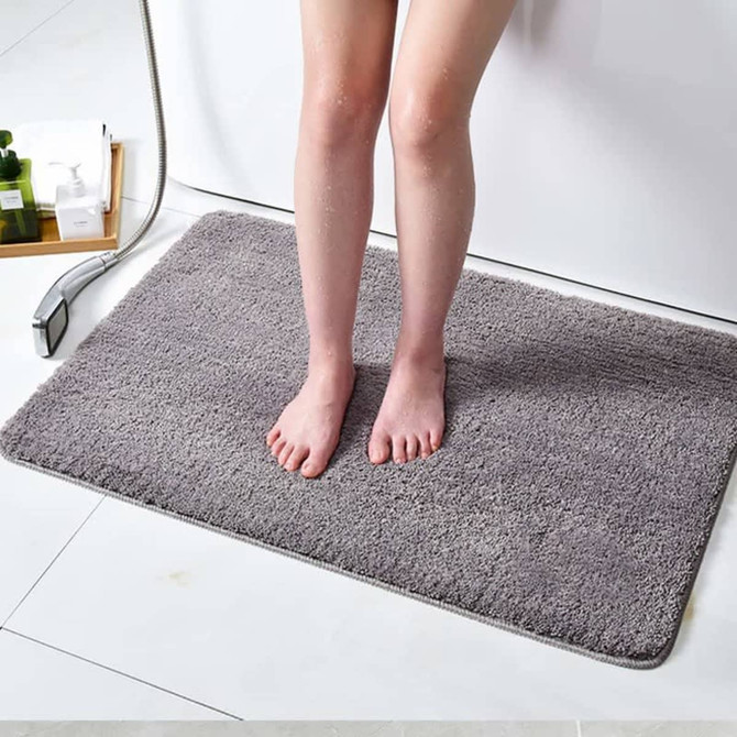 A grey flannel logo mat with soft texture, placed on a bathroom floor next to a shower.