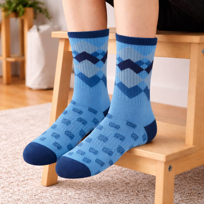 Blue crew socks featuring a chevron pattern and playful designs, displayed on a person's feet while seated on a chair.