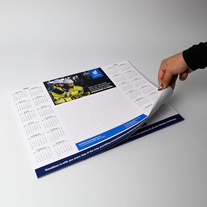 A3 notepad in white and blue, featuring a calendar layout and a section for notes, held by a hand.