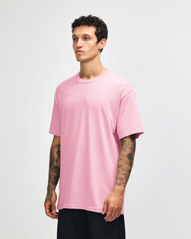 A pink heavyweight cotton unisex T-shirt displayed on a model, featuring a relaxed fit and short sleeves.