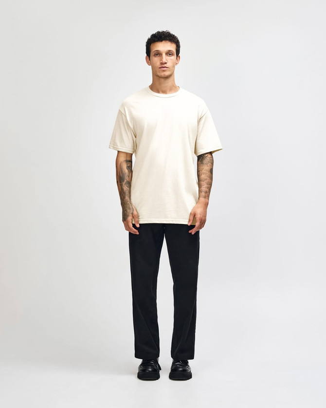 A model wearing a lightweight off-white unisex t-shirt paired with blue jeans and white sneakers, featuring a logo.