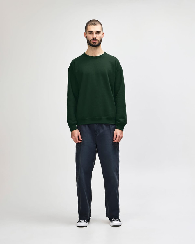 A green Gildan Heavy Blend adult crewneck sweatshirt worn by a model, paired with black jeans and sneakers.