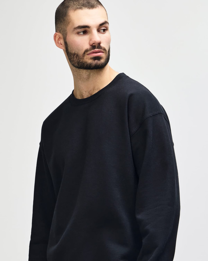 A black Gildan Heavy Blend Adult Crewneck Sweatshirt displayed on a model with long hair, crossing her arms.