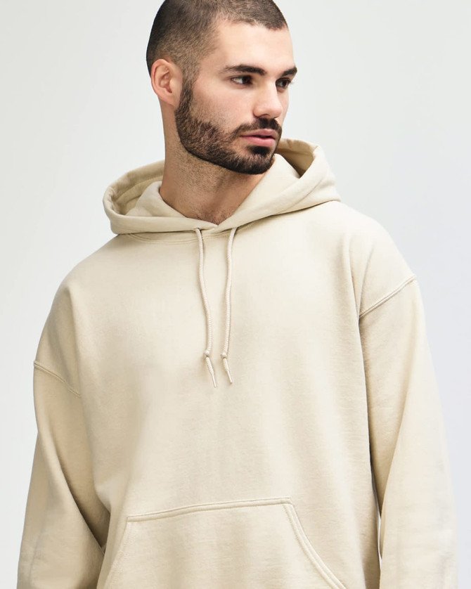 A beige hooded sweatshirt is modelled by a young woman with long hair, staring directly at the camera.